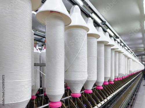 Row of white yarn spools on automated spinning cones in modern textile factory