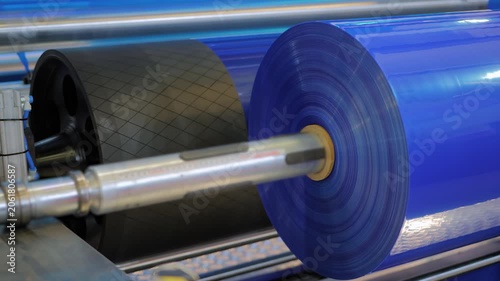 Close up view: automatic plastic film blowing machine - moving roller, winding roll with blue polyethylene film at exhibition, trade show. Recycling, industrial, manufacturing, and production concept