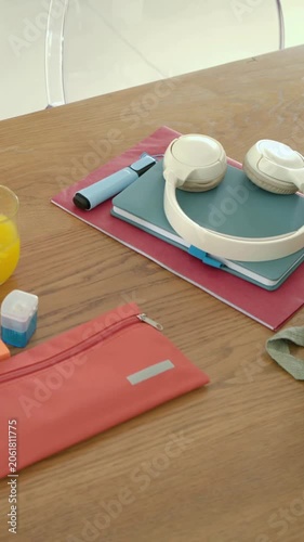 Vertical video: Panning camera revealing beige headphones on notebooks on table, showing bag strap