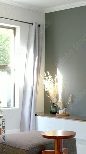 Vertical video: Sunlight driving camera panning across home corner showing gray ottoman, green vase