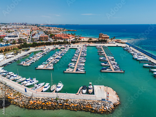 Aerial view of sunny coastal marina filled with boats and vibrant seasid of Torre de la Horadada town. Vacation, travel, and tourism, Mediterranean holidays and leisure activities. Costa Blanca, Spain