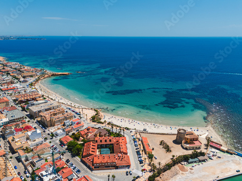 Aerial view of vibrant coastal town with sandy beach, residential buildings, clear blue Mediterranean Sea. Torre de la Horadada resort. Coastal tourism and vacation destination. Costa Blanca, Spain