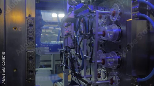 Automatic plastic injection molding machine is producing polypropylene sauce cups, containers, while pick and place robotic arm manipulator is removing the finished containers at the factory: close up