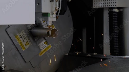 Automatic cnc laser cutting machine is working on cylindrical metal workpiece with many sparks at factory, plant. Industrial, manufacturing, metalworking, and equipment concept
