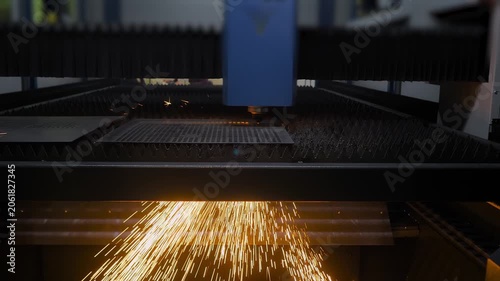 Automatic cnc laser cutting machine is operating on sheet metal with many sparks at factory, plant. Industrial, metalworking, technology, manufacturing, and equipment concept