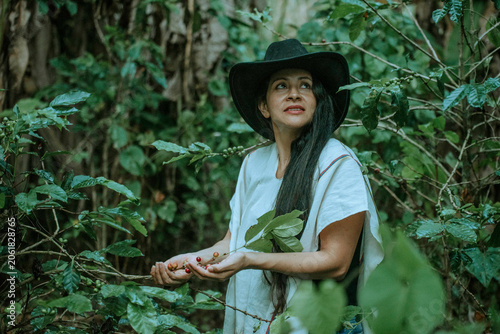 Portrait of a woman holding coffee cherries among lush coffee plants.