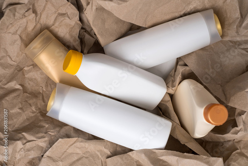 Collection of assorted empty plastic cosmetic bottles arranged on crumpled brown kraft paper, recycling concept