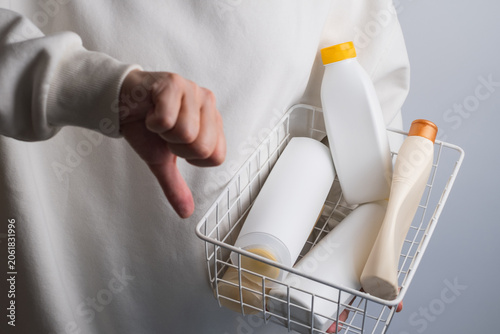 Person holding a basket full of plastic cosmetic bottles and showing a thumbs down gesture, plastic waste and pollution concept