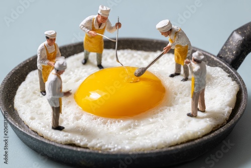 Miniature chefs preparing and cooking fresh fried egg in frying pan