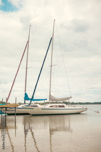 Sailing yachts with lowered sails moored beside a pier on a peaceful lake