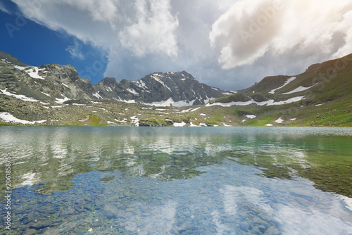 Clear mountain lake with a beautiful water reflection of rocky ridges and white clouds. Scenic alpine nature landscape