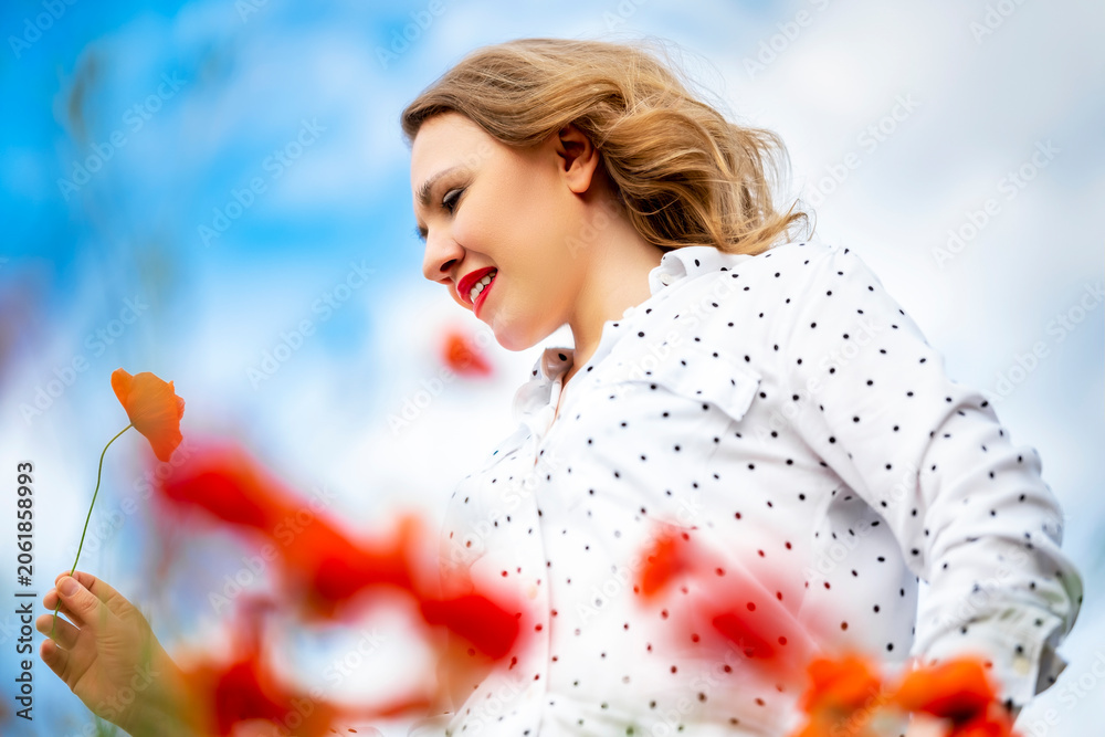 Fototapeta premium Content woman in polka dot blouse looking down at red poppy flower. Concept of mindfulness and appreciation of natural beauty.