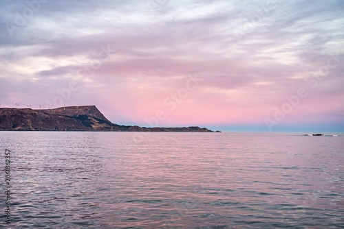 Scenic view of the water under a pink sky in Norway with distant cliffs and a quiet shoreline during sunset