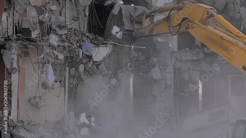 Yellow excavator with shovel bucket tearing down the old typical Turkish multi-storey apartment, residential building in Istanbul, Turkey - slow motion, demolition of building