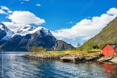 Lakeside or sea view in Norway with mountains, blue sky, and house by the water during a sunny day in spring or summer
