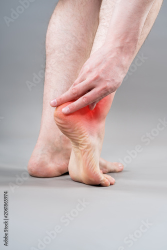 Heel pain, plantar fasciitis or achilles tendinitis concept. Rear view of man holding his aching foot with red inflammation graphic