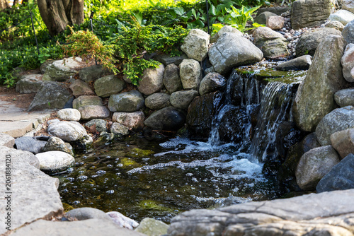 Small rocky waterfall feature with rocks and splashing stream in botanical garden pond. Mini cascade waterfall flowing over stones in park. Ornamental Gardens in Ottawa, Canada