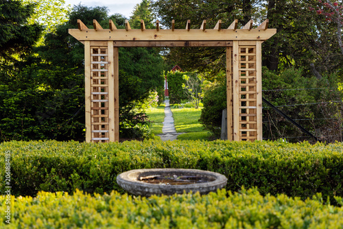 Stone birdbath in front of wooden garden pergola. Ornamental Gardens with arbor and pathway during spring in Ottawa, Canada