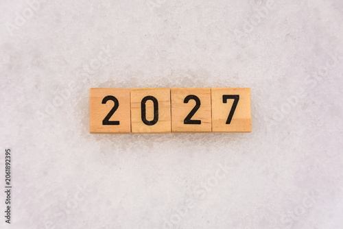The number 2027 is made of wooden blocks on a snowy background. Textured background with snow. New Year's concept.