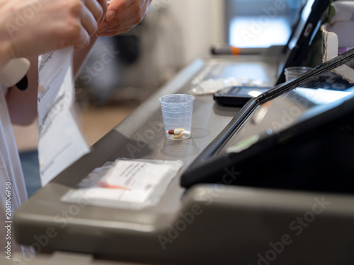Nurse holds a medication record beside a plastic cup with pills and a digital tablet on a care trolley during a medicine round.
