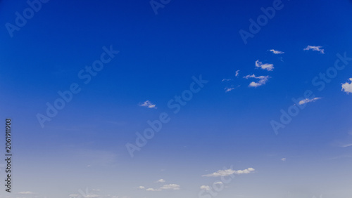 Minimalist view of a deep blue sky with scattered small white clouds. Clean natural background with ample copy space, suitable for weather, climate, travel, environmental and design concepts.