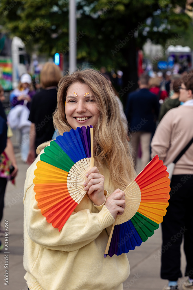 Naklejka premium Young woman with rainbow folding fans at 25th Warsaw Equality Parade (Parada Równości). LGBTQ pride, diversity, equality and inclusion concept