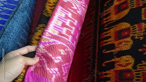 Hand touching rows of colorful traditional Thai silk fabrics, close up , Traditional Isan Thai silk fabrics featuring geometric and elephant patterns.