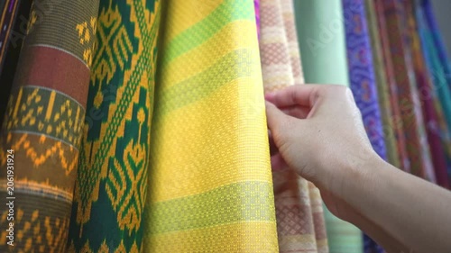 Hand touching rows of colorful traditional Thai silk fabrics, close up , Traditional Isan Thai silk fabrics featuring geometric and elephant patterns.