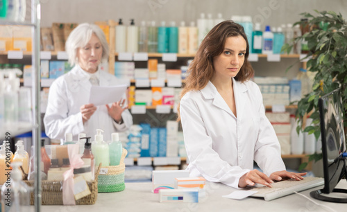 Fotografie Woman pharmacist is working at computer, reads indications for taking pills, sea