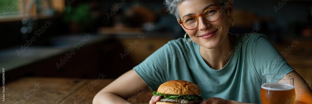 Fototapeta premium Older woman smiling while holding burger at dining table
