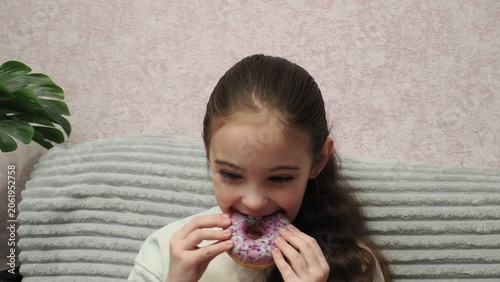 A portrait of a beautiful little girl holding a dessert—a donut covered in icing. A sweet expression on the girl's face as she enjoys a sweet donut. Diet for weight loss. Eating fast food and unhealth