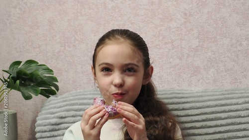 A portrait of a beautiful little girl holding a dessert—a donut covered in icing. A sweet expression on the girl's face as she enjoys a sweet donut. Diet for weight loss. Eating fast food and unhealth