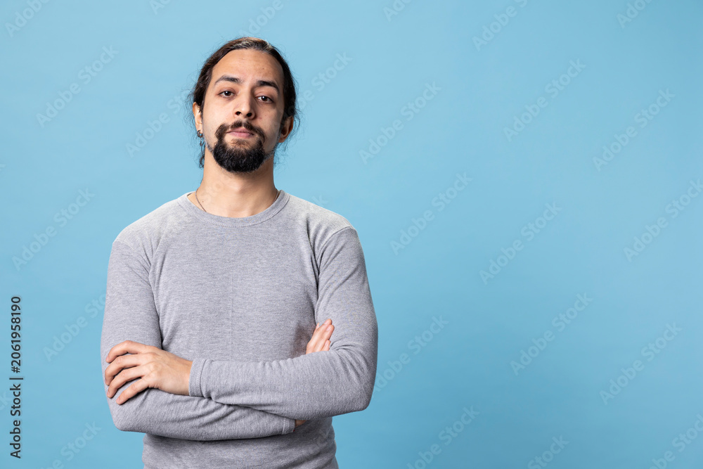 Fototapeta premium Male model with long curly hair posing with confidence in studio, standing with his casual wear against blue background. Young peaceful confident man with self assured attitude.