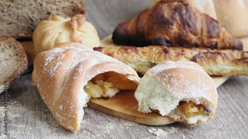 On the table are fresh bread and pastries, apple buns, pies, and croissants. Fresh, warm pastries topped with cheese are displayed in the bakery's display case.