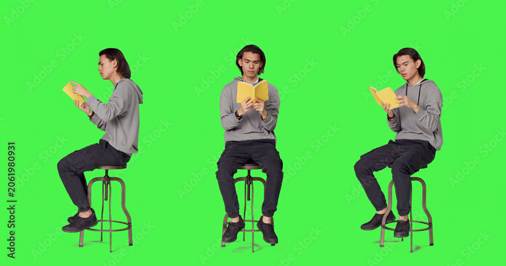 Obraz premium Trendy person reading novel book on chair against full body green screen template, enjoying old school lecture hobby, young asian adult holding literature or fiction book to read in studio
