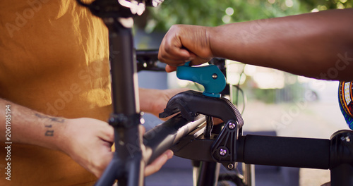 Foto Close-up shot of caucasian man carrying bike and African American woman clamping the frame to repair-stand for maintenance, interracial pair securing bicycle body for examining and fixing