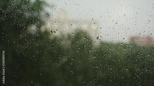 Large raindrops on the window during the rain against the background of the city