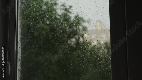 Large raindrops on the window during the rain against the background of the city