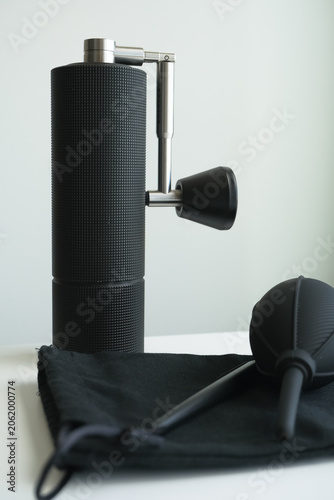 Quadro su tela Black manual coffee grinder with metal crank and cleaning tools on a cloth, arranged on a tabletop against a plain light background, coffee lovers
