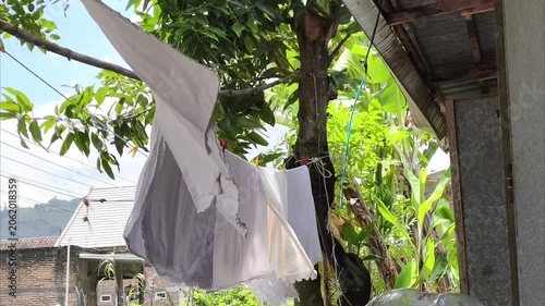 White laundry drying on a clothesline outdoors with green trees in the background.