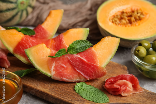 фотографія Wooden board of fresh melon pieces with delicious prosciutto and mint leaves on