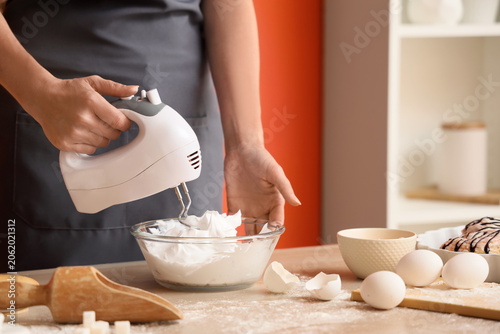 Obraz na plátně Woman whipping egg albumen with mixer at table in kitchen, closeup
