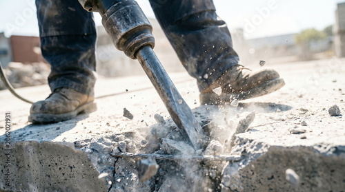 Jackhammer breaking concrete with debris flying at construction site, heavy labor and demolition work.