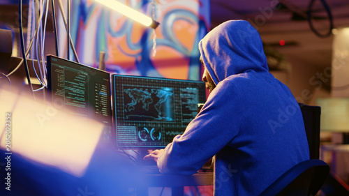 Billede på lærred African American hooded hacker hiding in underground base, anxiously looking around for threats, feeling nervous after stealing data from victims using virus, trying hard to evade law enforcement