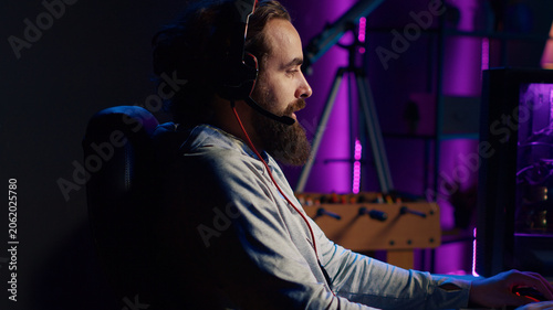 Cuadro en lienzo Close-up shot of man chatting with teammates online while playing video games on gaming PC, relaxing after work, gamer battling enemies in online multiplayer shooter, talking through headphones mic