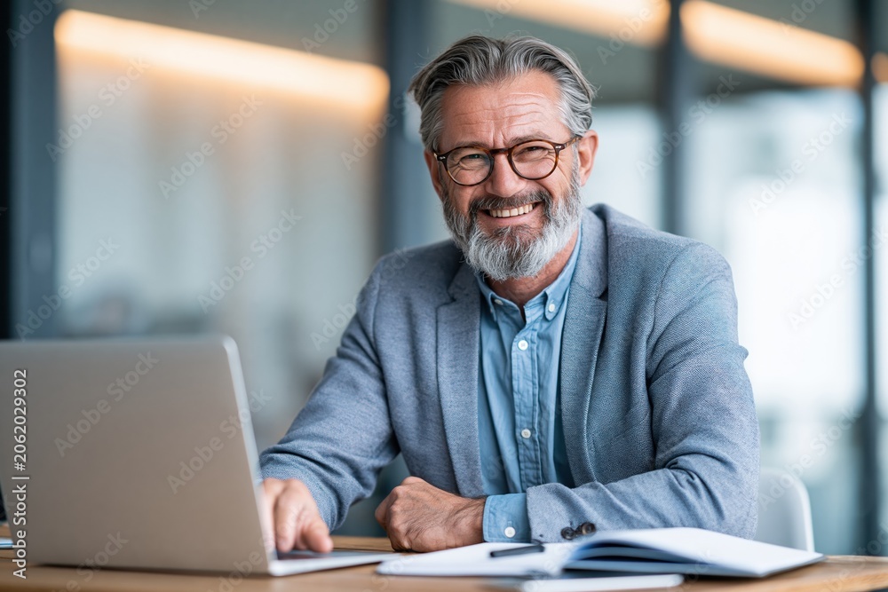 Fototapeta premium Smiling elderly man using laptop in modern office