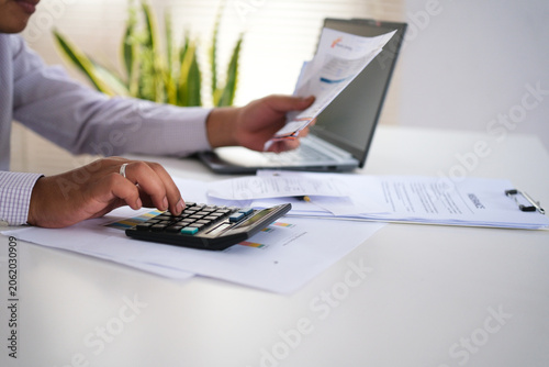 Fotografie Financial concept, a young businessman holding bills, calculating with a calculator