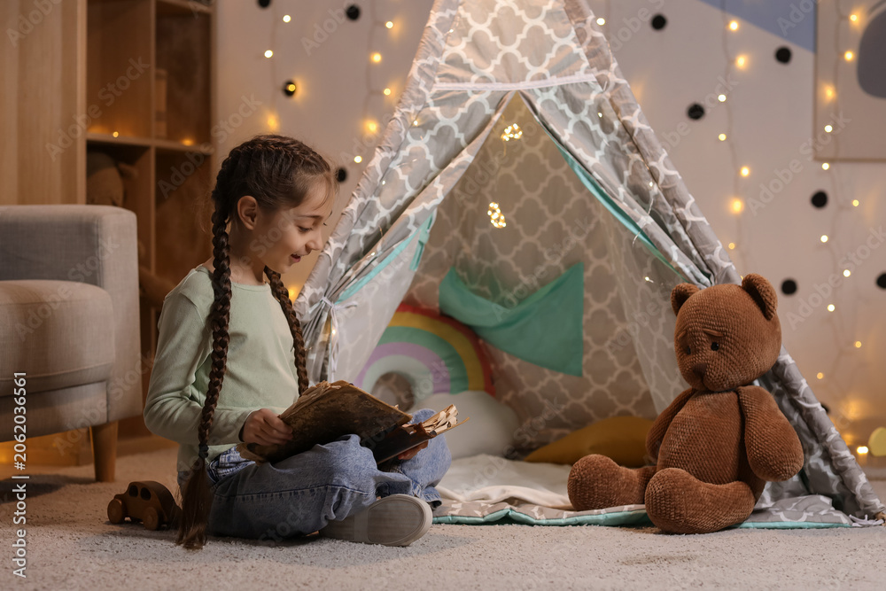Naklejka premium Cute girl reading adventure book at home in evening