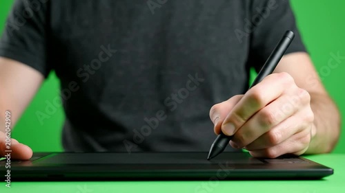 Close-Up of a Person's Hand Using a Stylus on a Graphic Tablet with Green Screen Background for Digital Art and Creative Projects