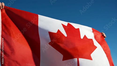 Close-Up Of A Person's Hands Holding A Vibrant High-Quality Canadian Flag Against A Clear Blue Sky Symbolizing National Pride And Identity